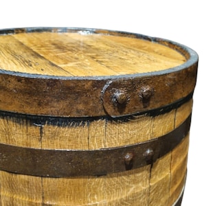 May include: Close-up of a wooden barrel with metal bands and rivets. The barrel has a light brown color with visible wood grain. The metal bands are dark brown, and the rivets are visible on the side.