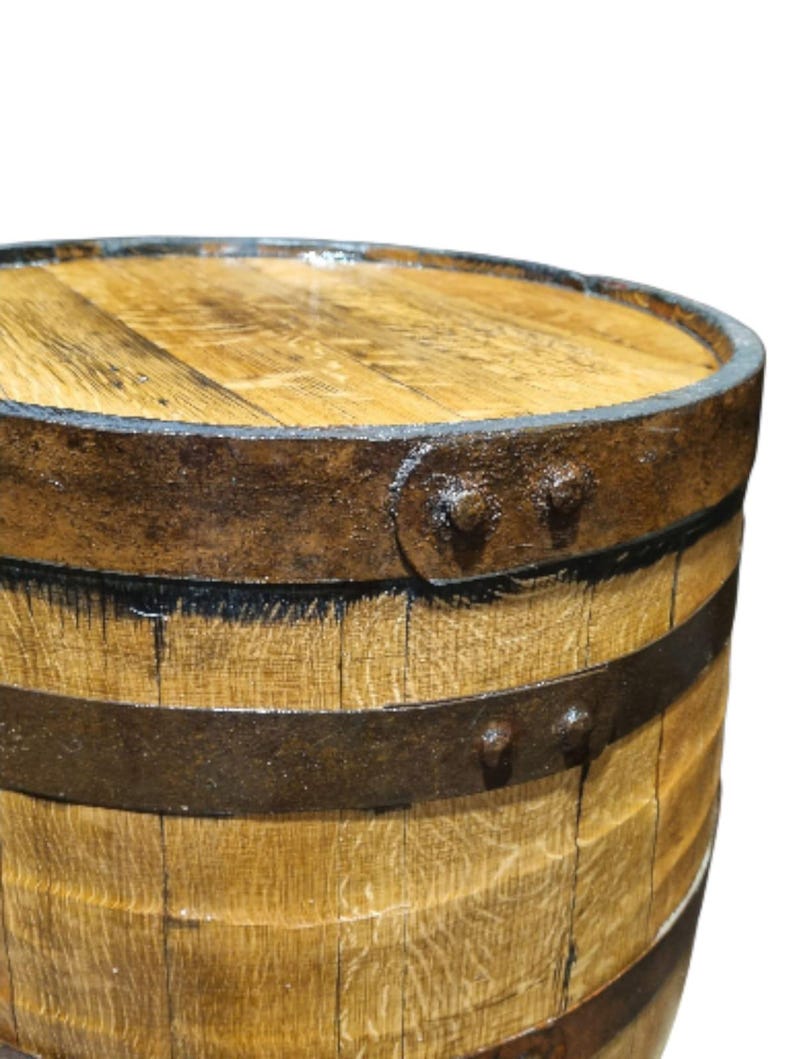 May include: Close-up of a wooden barrel with metal bands and rivets. The barrel has a light brown color with visible wood grain. The metal bands are dark brown, and the rivets are visible on the side.