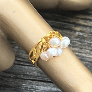 May include: A gold ring with a delicate design and a cluster of white pearls dangling from it.