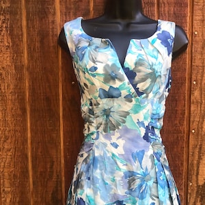 May include: Sleeveless floral dress in shades of blue, white, and gray. The dress features a V-neckline and a fitted bodice with a pleated skirt. The floral pattern includes large and small blooms.
