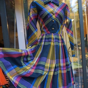 May include: A long-sleeved dress with a plaid pattern in shades of blue, purple, yellow, and red. The dress has a collared neckline and button closure.