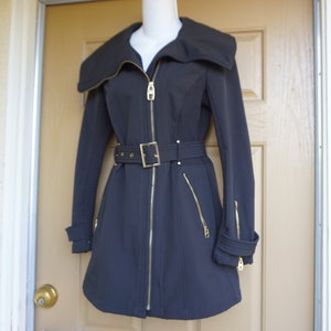 May include: A black coat with a wide collar and gold zippers. The coat features a belted waist and gold hardware. The sleeves have gold zippers at the cuffs. The coat is displayed on a mannequin.