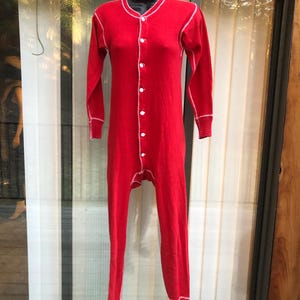 May include: A one-piece red thermal underwear set with long sleeves and legs. White stitching outlines the collar, cuffs, and seams. The front features white buttons for closure. The garment is displayed on a black mannequin.