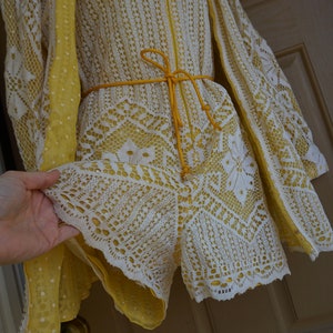 May include: A vintage romper with a matching cape, featuring a white lace overlay over a yellow lining. The romper has a zip-up front, short sleeves, and a yellow tie belt. The cape has a yellow polka dot lining.