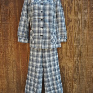 May include: A vintage plaid suit set, featuring a long-sleeved jacket with a collared neckline, two front pockets, and button closures. The matching wide-leg pants complete the ensemble. The suit is in a black, white, and gray plaid pattern.
