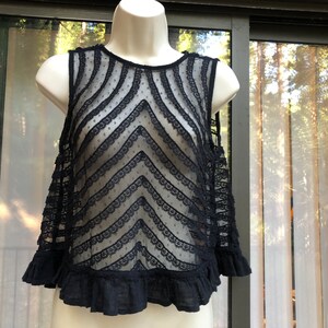 May include: Black lace sleeveless top with a scalloped trim and a chevron pattern. The top has a ruffled hem.