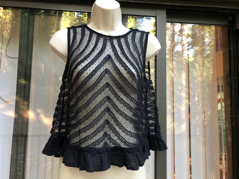 May include: Black lace sleeveless top with a scalloped trim and a chevron pattern. The top has a ruffled hem.