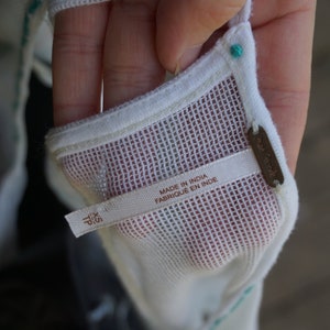 May include: Close-up of a white mesh top with turquoise embroidery and trim. The tag reads "Made in India" and "XS TP". A small brown tag with the brand name is also visible.