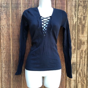 May include: A black long-sleeved shirt with a lace-up neckline. The shirt is fitted and has a v-neck.