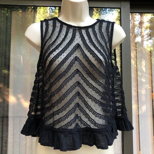 May include: Black sheer lace top with a ruffled hem and a chevron pattern. The top is sleeveless and has a round neckline.