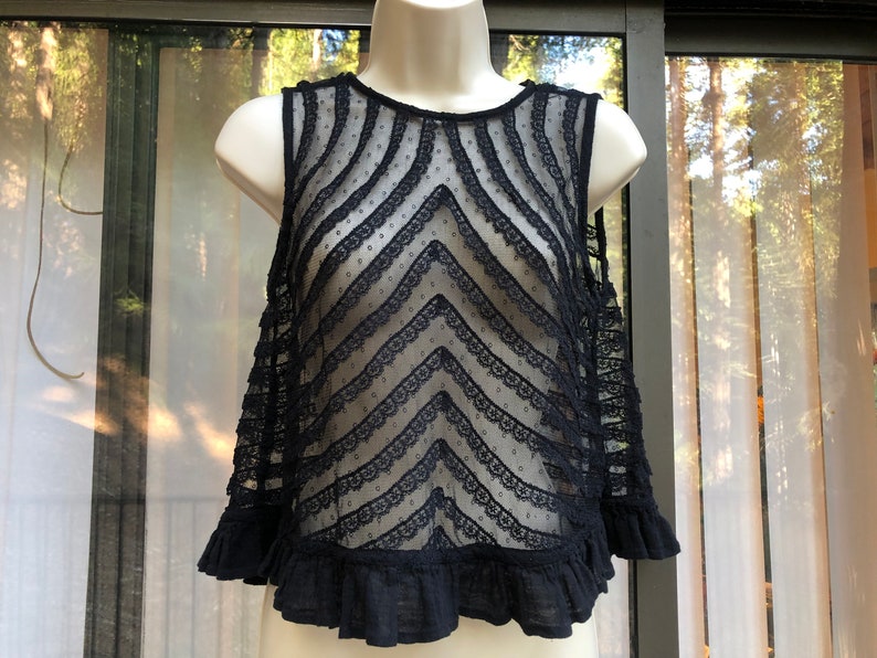 May include: Black sheer lace top with a ruffled hem and a chevron pattern. The top is sleeveless and has a round neckline.