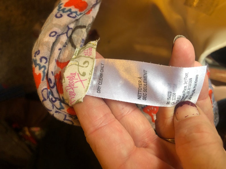 May include: A close-up of a patterned scarf with a tag that reads "Free People" and "Dry Clean Only." The scarf has a floral design with orange and blue accents. The tag also includes the text "NETTOYER A SEC SEULEMENT."
