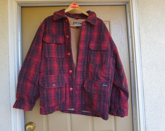 May include: Red and black plaid jacket with four front pockets and red buttons. The jacket is hanging on a wooden hanger. The jacket has a brown interior lining and a collar.