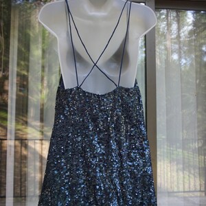 K&ouml;nnte beinhalten: Ein marineblaues Paillettenkleid mit Spaghettitr&auml;gern und tiefem R&uuml;ckenausschnitt h&auml;ngt an einer wei&szlig;en Schaufensterpuppe. Das Kleid ist mit kleinen, reflektierenden Pailletten bedeckt, die einen schimmernden Effekt erzeugen.