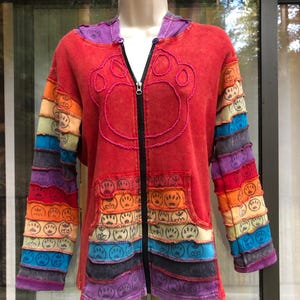 May include: Red zip-up hoodie with a paw print design on the front. The sleeves and pockets feature a rainbow pattern with paw prints. The hood is purple. A unique and colorful outerwear garment.