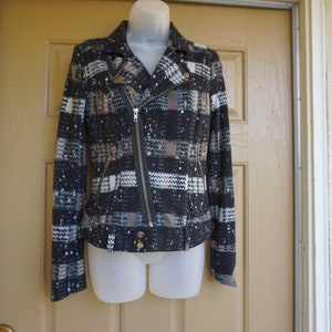 May include: A patterned jacket with a black, white, and brown design. The jacket features a diagonal zipper, a collar, and gold-colored buttons. The jacket is displayed on a mannequin.