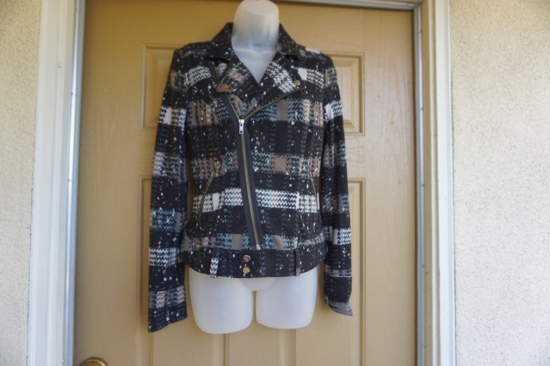 May include: A patterned jacket with a black, white, and brown design. The jacket features a diagonal zipper, a collar, and gold-colored buttons. The jacket is displayed on a mannequin.