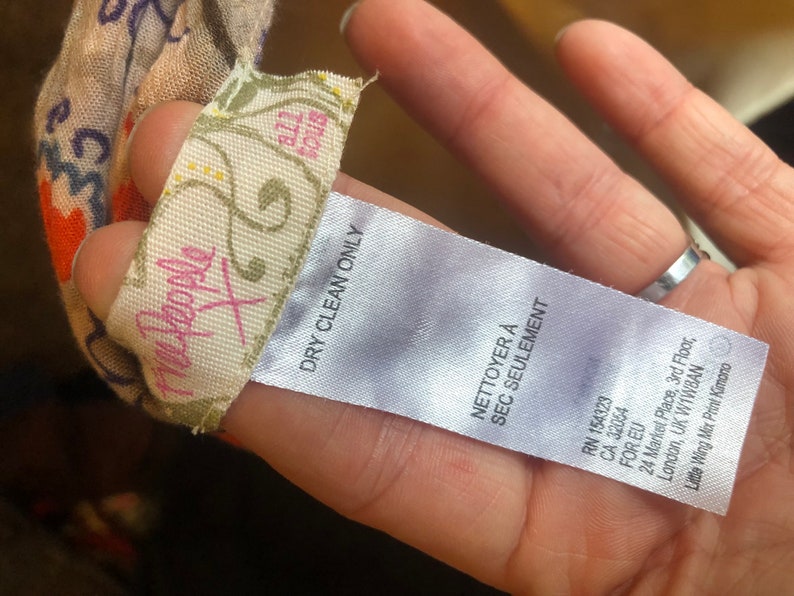 May include: A tag from the brand "Free People X" with the text "DRY CLEAN ONLY" and "NETTOYER &Agrave; SEC SEULEMENT". The tag is attached to a patterned fabric with orange, blue, and white floral designs.