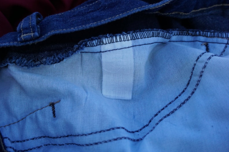 May include: Close-up of the inside of blue denim jeans. The image shows the waistband, the light blue lining, and the stitching details. A white label is visible.