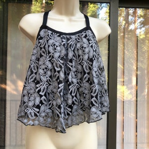 May include: A black and gray lace top with thin straps. The top has a scalloped hem and a floral pattern.
