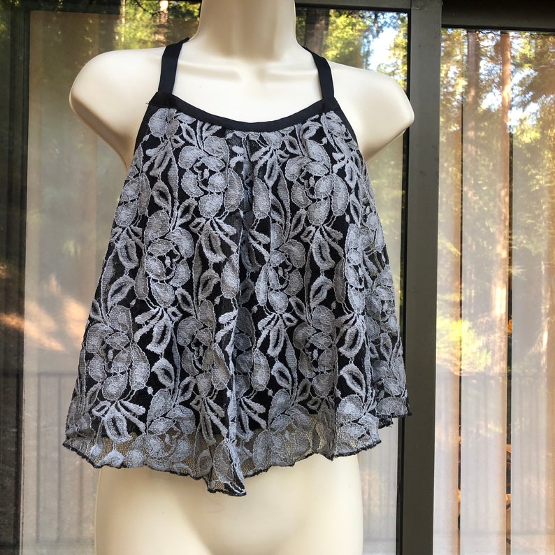 May include: A black and gray lace top with thin straps. The top has a scalloped hem and a floral pattern.