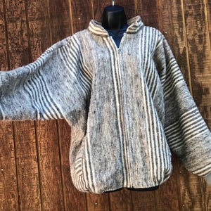 May include: A zip-up jacket featuring a textured grey and white striped pattern. The garment has long sleeves with ribbed cuffs, a high collar, and a full-length front zipper closure. The fabric displays a woven, heathered appearance throughout.