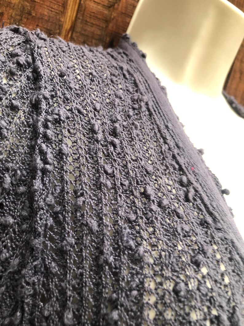 K&ouml;nnte beinhalten: Nahaufnahme eines dunkelblauen Strickkleidungsst&uuml;cks mit einem strukturierten, offen gewebten Design. Der Stoff hat ein Noppenmuster, das eine einzigartige, taktile Oberfl&auml;che erzeugt. Das Kleidungsst&uuml;ck ist &uuml;ber einer wei&szlig;en Schaufensterpuppe drapiert.
