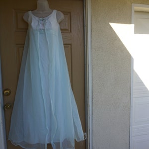 May include: A light blue vintage nightgown and robe set. The nightgown has a white bodice with a pink floral accent. The sheer robe drapes down to the floor. The set is displayed on a mannequin against a brown door.