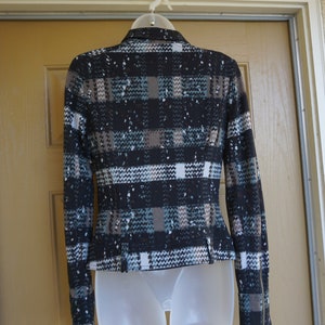 May include: A fitted jacket with a plaid pattern in black, brown, white, and teal. The jacket has a notched collar, long sleeves with zippers at the cuffs, and a tailored waist. It is displayed on a white plastic form.