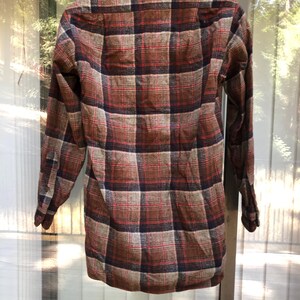 May include: A long-sleeved plaid shirt in shades of brown, red, and navy blue. The shirt features a classic button-down design with a collared neckline and cuffs. The plaid pattern is a traditional design.