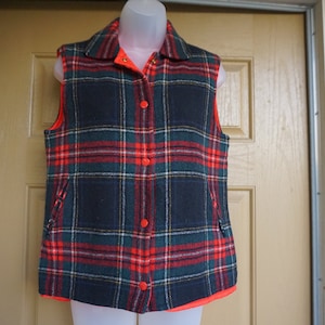 May include: A plaid vest in navy, red, and green, with a bright orange lining and buttons. The vest has a collared neckline and two front pockets. This vintage vest is a classic outerwear piece.