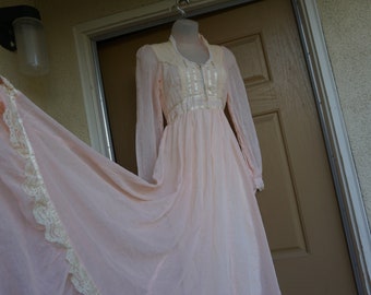 May include: A long, flowing, pink dress with a white lace trim. The dress has long sleeves and a high neckline. It is made of a sheer fabric and has a vintage style.