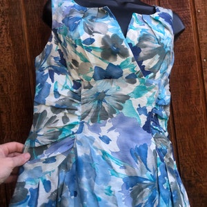 May include: Sleeveless dress with a floral pattern in shades of blue, gray, and white. The dress features a V-neckline and a fitted bodice with pleating details. The skirt is flared, and the fabric appears to be lightweight.