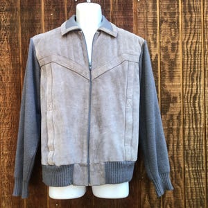 May include: A gray suede and knit jacket with a full zipper closure. The jacket features a gray suede front panel with decorative stitching and gray knit sleeves and hem. The jacket is displayed on a mannequin.
