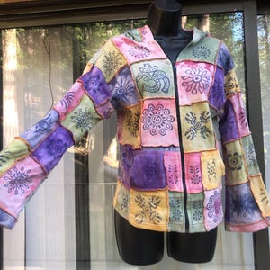 May include: Patchwork zip-up hoodie in a variety of colors including pink, purple, yellow, and green. The jacket features a hood, long sleeves, and a black zipper. The design includes floral and Om symbols.
