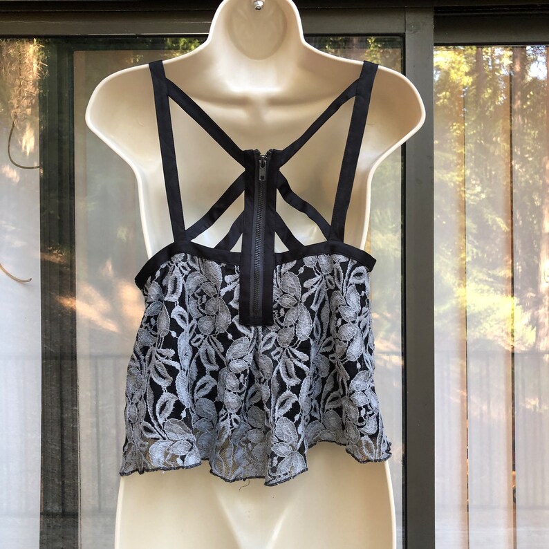 May include: A black and white lace crop top with a black criss-cross strap back and a zipper closure.