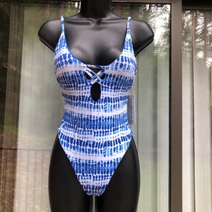 May include: A blue and white tie-dye swimsuit with a keyhole cutout and criss-cross detail at the bust. The one-piece swimsuit has thin straps and a high-cut leg. The swimsuit is displayed on a black mannequin.
