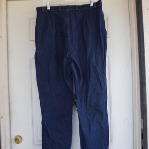 May include: Dark blue denim trousers hanging on a white hanger. The trousers have a straight leg cut and a classic five-pocket design. The denim appears to be a medium weight, suitable for various seasons.