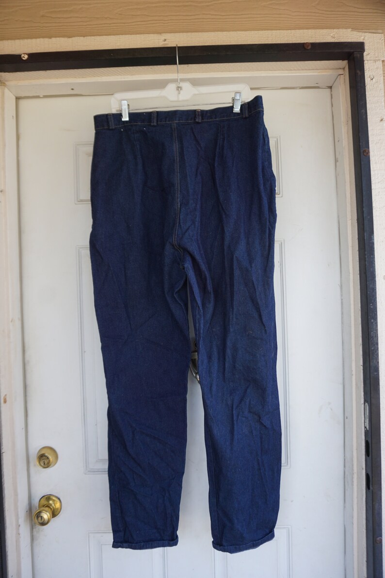 May include: Dark blue denim trousers hanging on a white hanger. The trousers have a straight leg cut and a classic five-pocket design. The denim appears to be a medium weight, suitable for various seasons.