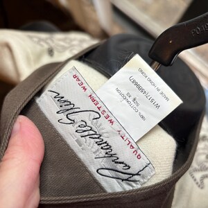 Puede incluir: Primer plano de una prenda Western wear marr&oacute;n y beige. La etiqueta dice "Vanhandle Glim QUALITY WESTERN WEAR". Una etiqueta indica que la prenda es XS, 100% algod&oacute;n y fabricada en Hong Kong.