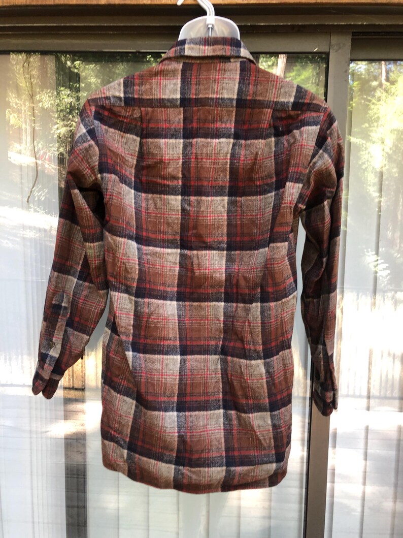 May include: A long-sleeved plaid shirt in shades of brown, red, and navy blue. The shirt is hanging on a white hanger, showcasing the back of the garment. The plaid pattern is a classic design, suitable for casual wear.