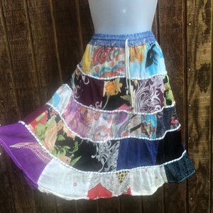 Puede incluir: Una falda de retazos colorida con una cintura de mezclilla y un cordón blanco. La falda está hecha de varias telas en tonos de morado, azul, blanco, negro y verde.