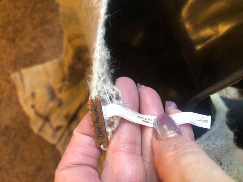 May include: A close-up of a white Free People sweater with a brown tag that says "Free People" and a white tag that says "Made in China".