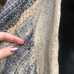 May include: A close-up of a blue and beige knitted scarf with a small hole in the fabric.