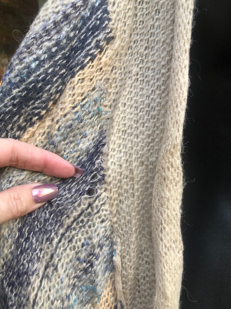 May include: A close-up of a blue and beige knitted scarf with a small hole in the fabric.