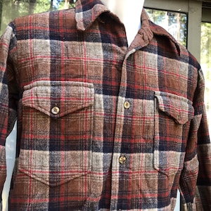 May include: A brown, red, and navy plaid flannel shirt with two button-flap chest pockets. The shirt has a collared neckline and button closures. The fabric has a textured appearance.