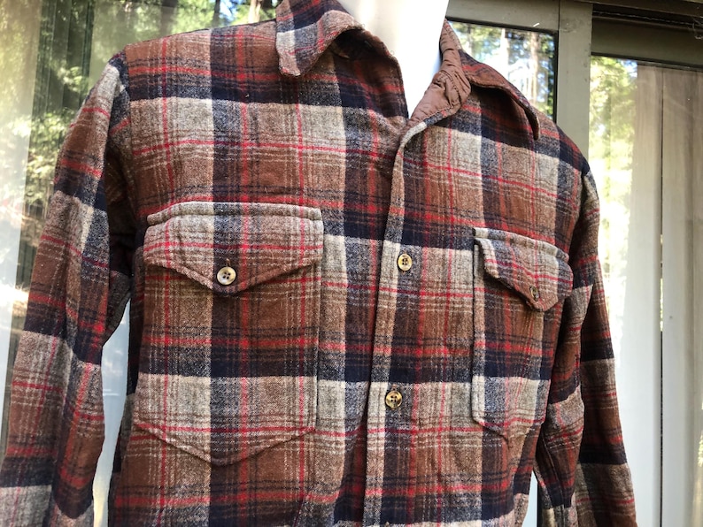 May include: A brown, red, and navy plaid flannel shirt with two button-flap chest pockets. The shirt has a collared neckline and button closures. The fabric has a textured appearance.