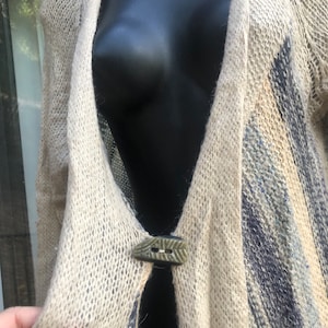 May include: A beige knitted cardigan with a blue and white pattern. The cardigan has a single button closure with a green and brown design.
