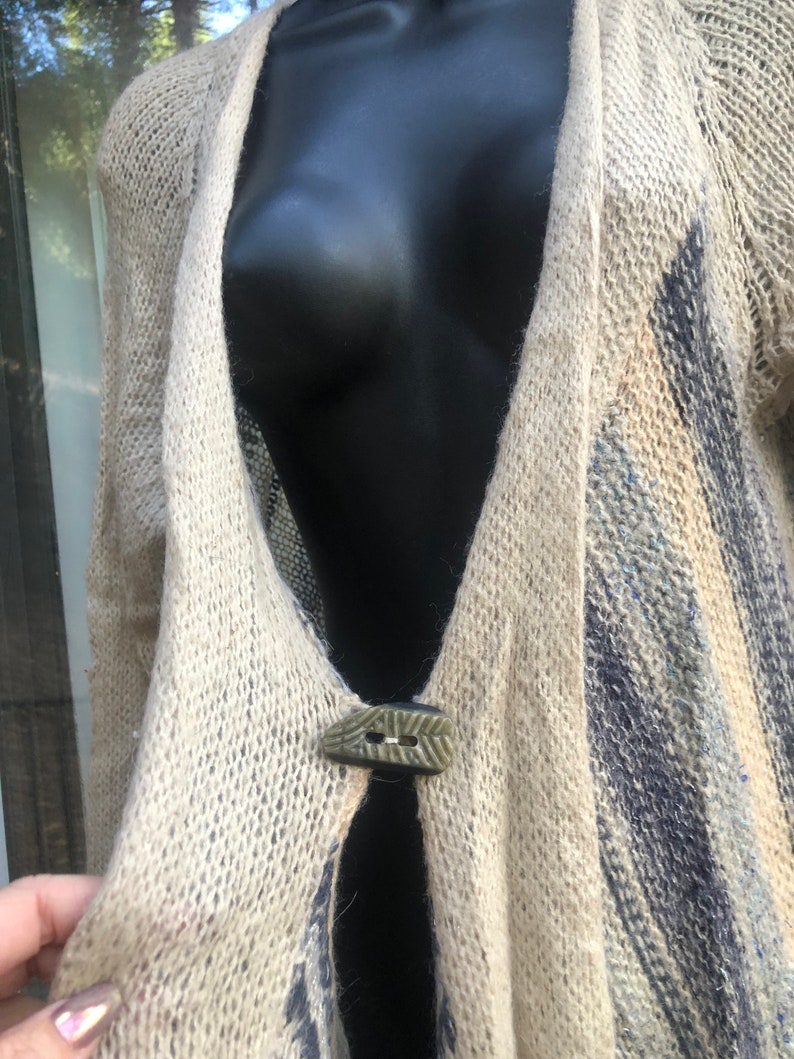 May include: A beige knitted cardigan with a blue and white pattern. The cardigan has a single button closure with a green and brown design.