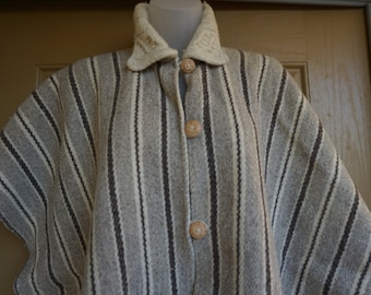 May include: A gray and white striped poncho with a cream-colored collar and wooden buttons. The poncho has a button-up front and a textured, woven appearance. The collar is a lighter shade of cream and has a knitted design.